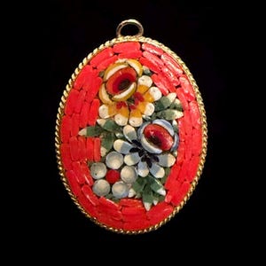 May include: An oval pendant featuring a micro-mosaic floral design. The center displays yellow, white, and blue flowers with green leaves, surrounded by a border of small, rectangular red pieces. The entire piece is set in a gold-toned twisted metal frame.