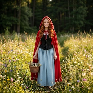 May include: A person wearing a red hooded cloak, black corset, and a long blue skirt, holding a woven basket filled with flowers. The person is standing in a field of wildflowers with a forest in the background. The cloak is a vibrant red.