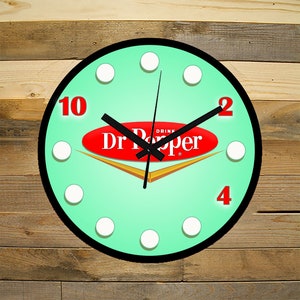 May include: A round, mint green wall clock with a black rim and white dots around the edge. The clock face features a red oval with the text "Drink Dr Pepper" in white. The clock hands are black and the numbers are red.