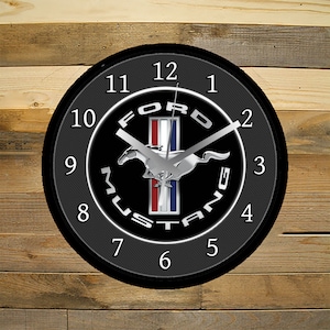 May include: A black and silver Ford Mustang clock with a black background and white numbers. The clock has a silver horse and the words "Ford Mustang" around the outside.