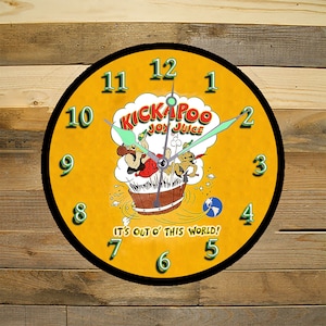May include: A yellow and black round clock with a cartoon image of two figures in a barrel. The clock face has black numbers and hands. The text "KICKAPOO JOY JUICE" and "IT'S CUT O' THIS WORLD!" are printed on the clock face.