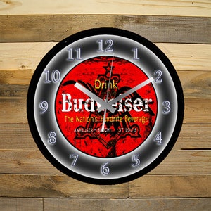 May include: A black and silver wall clock with a red, white, and yellow Budweiser logo. The clock face has a distressed look and the text "Drink Budweiser The Nation's Favorite Beverage Anheuser-Busch St. Louis" is printed on the face.