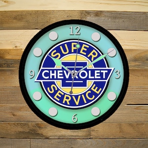 May include: A round clock with a black face and white numbers. The clock has a blue and yellow logo in the center that says "Super Chevrolet Service". The background of the clock is a light blue and green gradient.