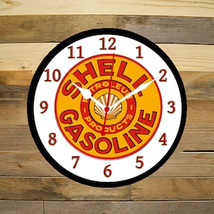 May include: A white and black clock with a red and yellow Shell Gasoline logo. The clock face has black numbers and hands.