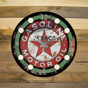 May include: A round, black-framed clock with a red, white, and green Texaco gasoline logo. The clock face has a white background with black numbers and a red star in the center. The clock hands are silver.