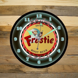 May include: A black and white clock with a red, yellow, and white Frostie Root Beer bottle cap design. The clock face has a neon green glow around the numbers and the text "Time for a Frostie! Drink Root Beer You'll love it!"