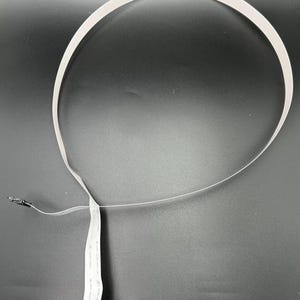 May include: White flat ribbon cable with a black connector on each end. The cable is coiled into a circle.