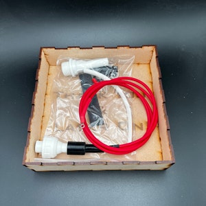 May include: A wooden box containing two white and black electrical connectors, a red wire, and a white wire. The box is labeled "The Tank On".