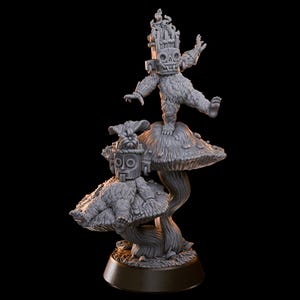 Może przedstawiać: Szara rzeźba przedstawiająca dwie postacie na grzybach. Postacie mają stylizowane twarze i nakrycia głowy. Jedna postać stoi, druga siedzi. Rzeźba ma ciemną podstawę i czarne tło.