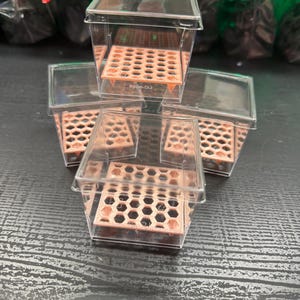 Puede incluir: Un conjunto de cuatro recipientes cuadrados de plástico transparente, cada uno con un inserto extraíble de color melocotón con un patrón hexagonal de panal. Los recipientes están apilados y agrupados, con el texto RC-0022 visible en los insertos.
