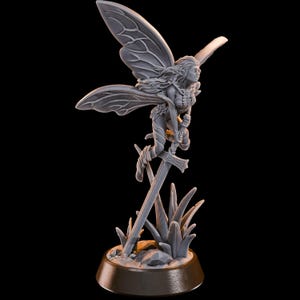 May include: A grey fairy figurine with detailed wings, holding a sword, and perched above stylized grass. The fairy is depicted in a dynamic pose, with flowing hair and intricate detailing on the wings and clothing. The base is a dark brown colour.