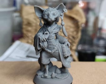 May include: A grey figurine of a humanoid creature with large ears, wearing ornate clothing and holding a pouch. The figure is standing on a round base with a gold rim, and has detailed facial features.