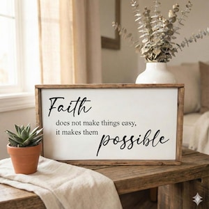 May include: Wooden framed sign with the words "Faith does not make things easy, it makes them possible" in black script. A small potted succulent and a vase with dried flowers are also visible.