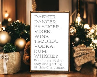 May include: A rectangular wooden sign with a white background and black text listing the names Dasher, Dancer, Prancer, Vixen, Wine, Tequila, Vodka, Rum, Whiskey, followed by the phrase Rudolph isn't the only one getting lit this Christmas.