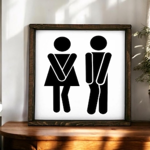 May include: A black and white sign with a wooden frame. The sign features two stick figures, one with a skirt and the other with pants. The figures are facing forward and have their arms crossed.
