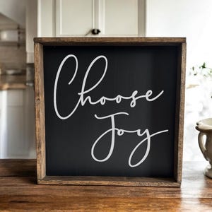 May include: A wooden sign with a black background and a white inscription that reads "Choose Joy".