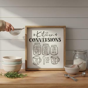 May include: A framed kitchen conversions sign with a wooden frame. The sign displays measurements for volume conversions, including gallons, quarts, pints, cups, and ounces. A stack of bowls, a jar of flour, and measuring spoons are on the wooden surface.