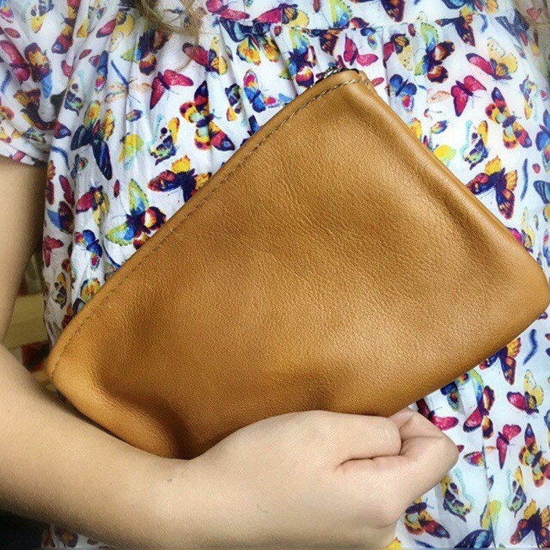 May include: A brown leather clutch purse with a zipper closure.