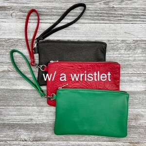 May include: Three leather wristlet clutches in black, red, and green. The red clutch has an embossed floral design and the text "w/ a wristlet".