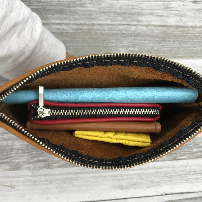 May include: A brown leather zippered pouch with a black zipper. The pouch is open and contains a blue phone case, a red wallet, and a yellow pouch.