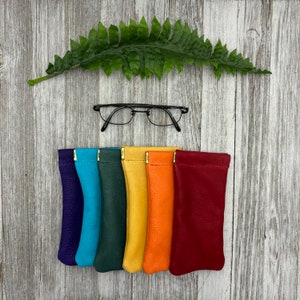 May include: Six colorful leather eyeglass cases lined up in a row. The cases are purple, turquoise, green, yellow, orange, and red.