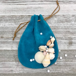 May include: Teal suede drawstring pouch decorated with seashells and white beads.