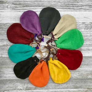 May include: Ten small, colorful suede pouches with drawstrings. The pouches are arranged in a circle on a light wood background.
