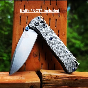 May include: A silver pocket knife with a black and white patterned handle. The knife has a blue screw on the handle and a blue screw on the blade. The text "Knife *NOT* Included" is written on a wooden surface behind the knife.