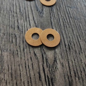 May include: A pile of 12 gold-colored metal washers, and two more washers are separated from the pile on a wood surface.