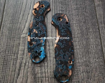 May include: Two custom knife scales with a unique blue, brown, and copper-colored pattern. The scales have multiple holes and a circular opening at the base. The text "DNALASERING.COM" is visible.
