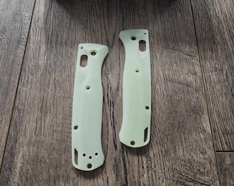 May include: Two pale green, contoured knife handle scales featuring pre-drilled holes for assembly, positioned below a blue Benchmade Knife Company box with white text. The scales have a smooth, matte finish and specific cutouts for hardware.