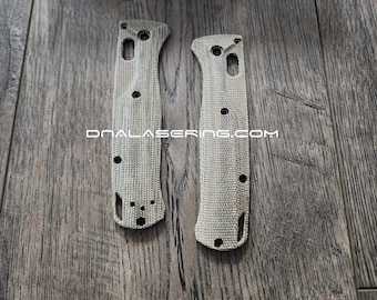 May include: Two textured knife handle scales with multiple holes and a cutout, in a light gray color. The text "DNALASERNG.COM" is printed on the scales. A blue box with the word "BENCHMADE" is in the background.