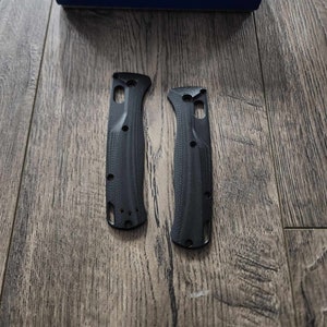 May include: Two black knife scales with a textured pattern. The scales are made of a durable material and are designed to fit a Benchmade knife.