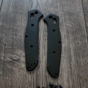 Può includere: Due guance di coltello nere con un set di viti nere. Le guance sono realizzate in un materiale liscio e duro e hanno una forma leggermente curva.