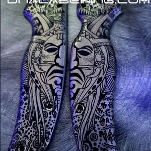 Puede incluir: Un par de mangos de cuchillo con patrones en blanco y negro con diseños intrincados. Los mangos presentan una cara estilizada con patrones geométricos y un patrón repetitivo de puntos y espirales.