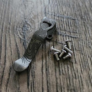 Puede incluir: Un cuchillo de bolsillo negro y plateado con un mango estampado y un pequeño juego de tornillos.