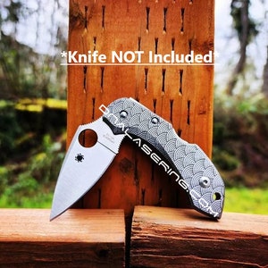 May include: A silver folding knife with a patterned handle, set against a wooden background. The handle features a wave-like design in black and white. The text "*Knife NOT Included*" is visible.