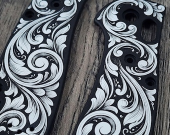 Könnte beinhalten: Zwei schwarze Messergriffschalen mit detaillierten, weiß lasergravierten Rankenmustern. Die Schalen haben vorgebohrte Löcher für die Montage und der Text DOALASERING.COM ist auf dem linken Teil sichtbar. Das Design zeigt fließende Blattformen.