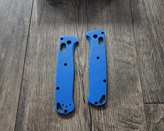 May include: Two blue plastic knife scales for a Benchmade knife. The scales are smooth and have a rounded shape.