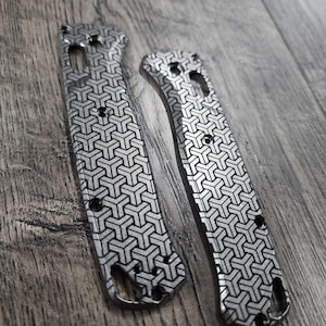 May include: Two silver knife scales with a geometric pattern. The scales are made of metal and have a black and silver finish.