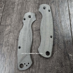 May include: Two light grey knife handle scales with a textured surface and multiple drilled holes. The scales are made of a durable material and are designed to fit a folding knife. The text "ONALASERING.COM" is visible on the bottom scale.