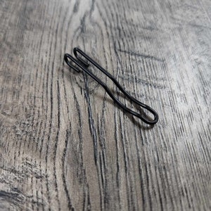 May include: A black metal clip with a curved shape. The clip is designed to hold items together.