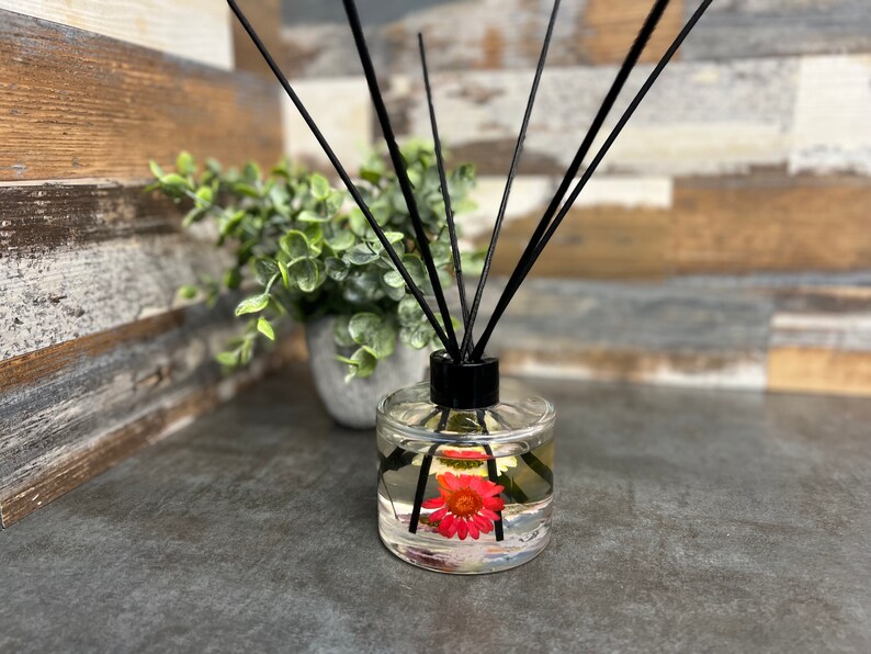 May include: A clear glass diffuser bottle with a black lid and black diffuser sticks. The bottle contains a clear liquid with a pink flower inside.