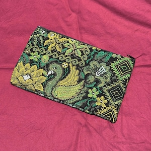 May include: A rectangular beaded clutch featuring a peacock design in shades of green, yellow, and black. The clutch has a zipper closure and a detailed floral and geometric pattern.