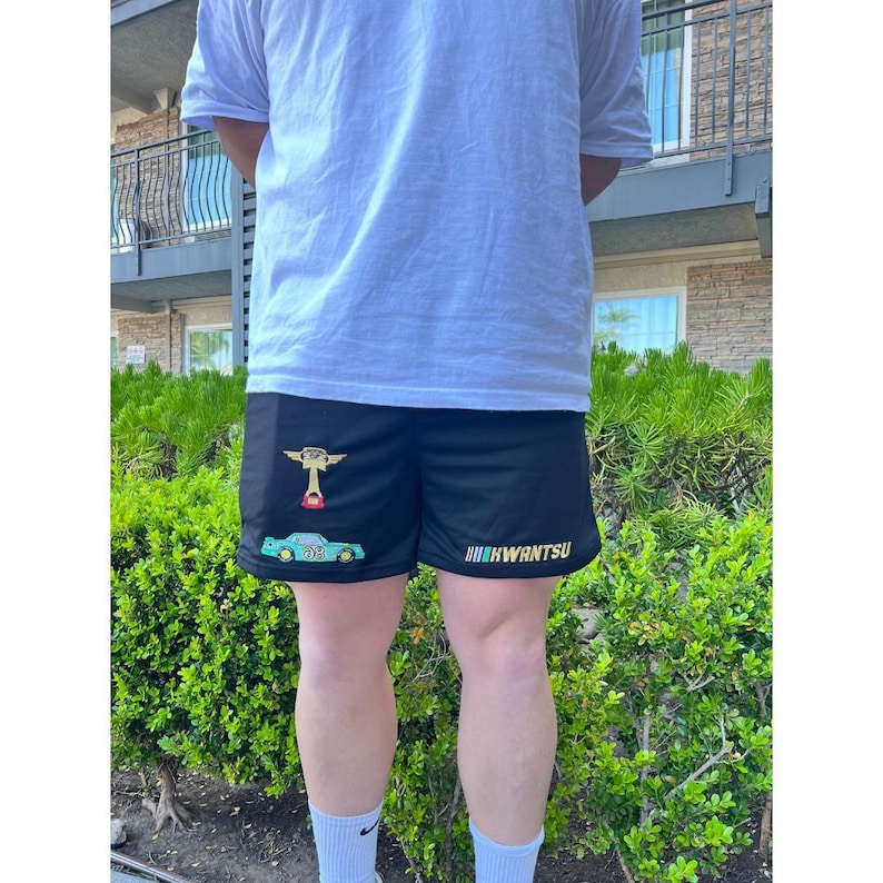 May include: Black athletic shorts with a green car and a cartoon character graphic on the left leg. The text "HWANTSU" is printed on the right leg.