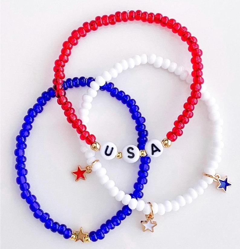 May include: Three beaded bracelets in red, white, and blue, with the letters "USA" spelled out on one. Each bracelet has a star charm. The bracelets are a patriotic accessory.