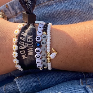 K&ouml;nnte beinhalten: Eine Sammlung von Armb&auml;ndern mit Perlen und ein schwarzes Armband mit wei&szlig;em Text, der "MORGAN WALLEN" lautet. Die Armb&auml;nder umfassen bl&uuml;tenf&ouml;rmige Perlen, Buchstabenperlen mit der Aufschrift "KICK MYSELF WALLEN" und ein wei&szlig;es Armband mit einem goldenen Anh&auml;nger.