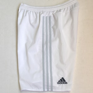 May include: White athletic shorts with three grey stripes down the sides and an Adidas logo on the right leg.