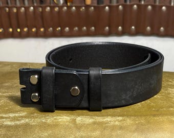 May include: A black leather belt with a silver buckle and rivets. The belt is rolled up and lies on a gold-colored surface. A brown leather tool roll with various tools is in the background.