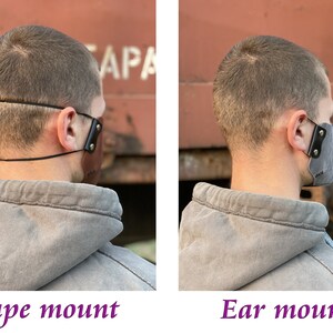 May include: Two images showing two different ways to wear a leather face mask. The first image shows the mask worn with a strap that goes around the back of the head. The second image shows the mask worn with straps that go over the ears. Both images show the mask worn by a person with short brown hair.